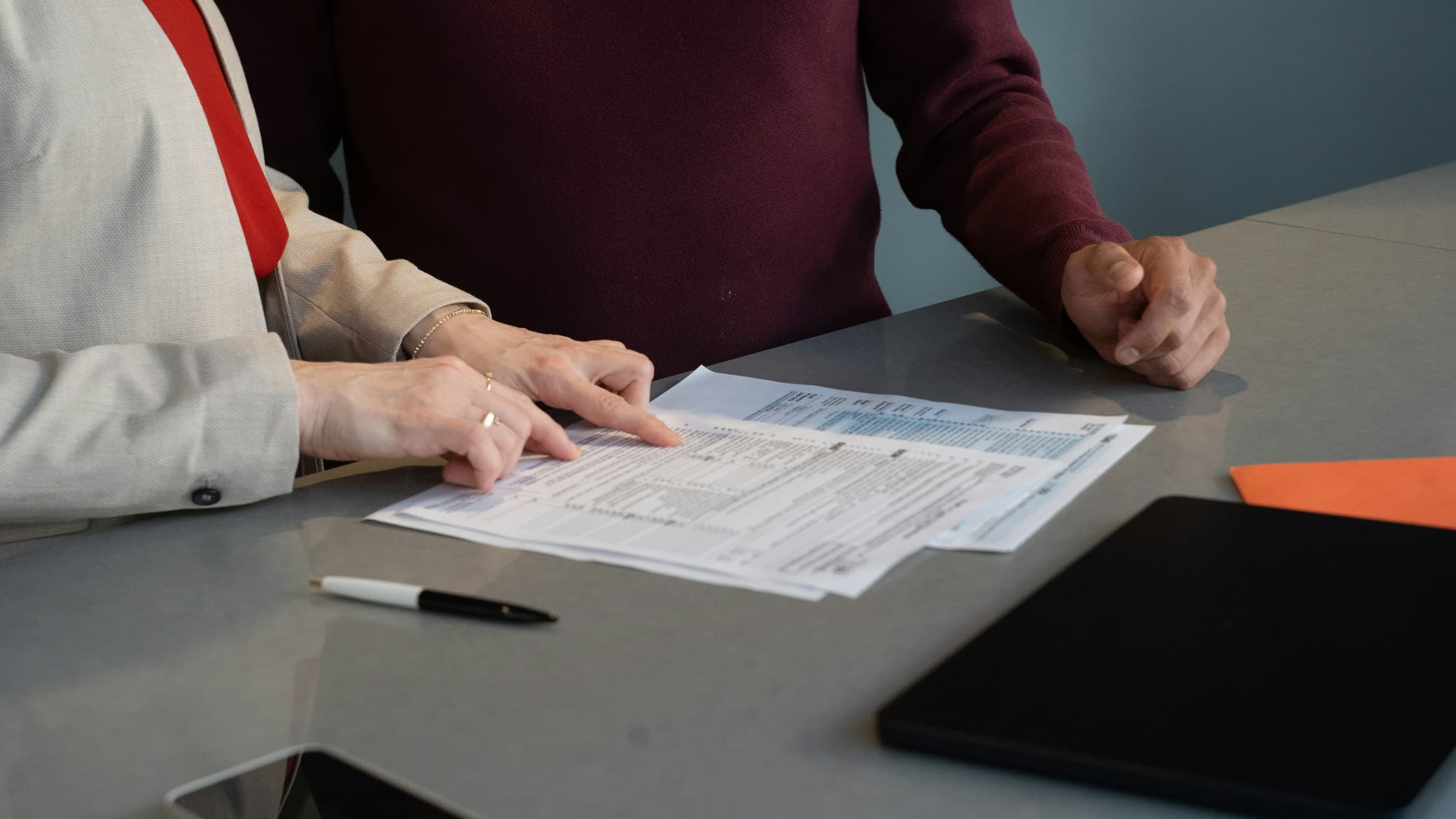 Two people at a table, one pointing to a line on a printed page.