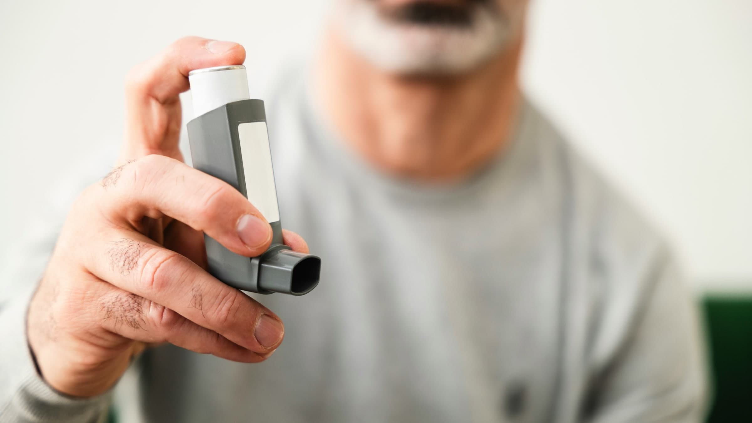 A man holds up an inhaler toward the camera.